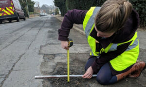 співробітник комунальної служби вимірює глибину ями на дорозі